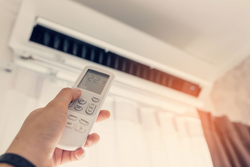 Air conditioner inside the room with woman operating remote controller.