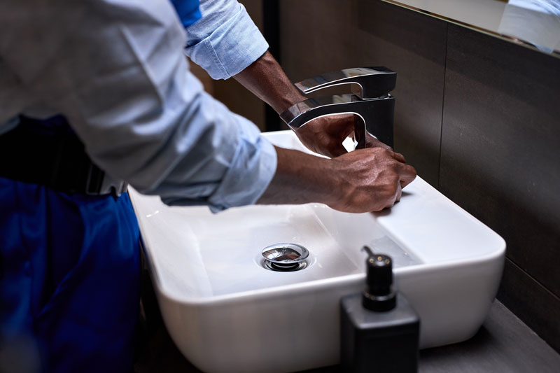 Professional handyman or plumber in blue uniform is repairing installing water tap crane.